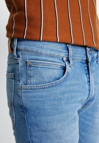 Blå denimjeans med en ljus tvätt, med en åtsittande design, fem fickor och kontrasterande sömmar.