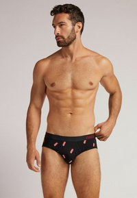 Schwarze Baumwollunterhosen mit roten Coca-Cola-Logo-Akzenten, ausgestattet mit einem bequemen Bund und einem figurverleihenden Design. Glatte Textur und klassisches Format.