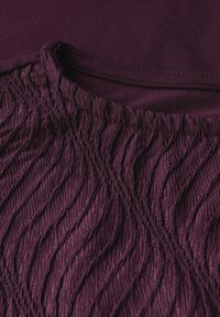 Burgundy fabric featuring a textured, pleated design with wavy lines and subtle stitching details. Smooth material at the top.