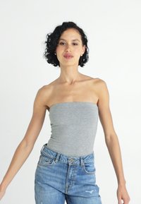Grå stroppeløs bodysuit laget av mykt stoff, kombinert med høy midje slitte blå jeans, med en avslappet passform og synlig søm.