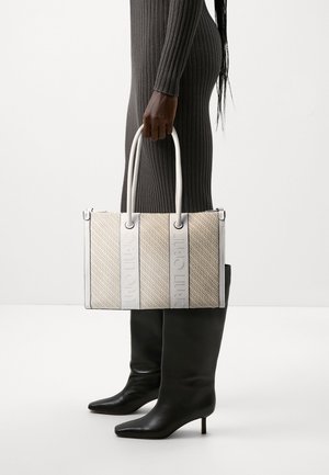 Bolso de mano tejido beige con acentos de cuero blanco y logo grabado. Forma rectangular, doble asa y patrón texturizado. Botas negras hasta la rodilla.