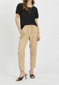 Top corto a maniche corte in tessuto nero, abbinato a pantaloni beige a sigaretta e mule nere con tacco. L'outfit presenta una cintura elastica sui pantaloni.