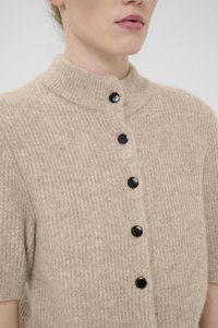 Beige strikket cardigan med høy krage, med en fem-knapps lukking med svarte glansknapper og korte ermer. Teksturert stoffdetalj.