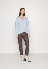 Helles, blaues Strickpullover mit V-Ausschnitt, kombiniert mit braunen, falschen Lederhosen und cremefarbenen Knöchelstiefeln mit Blockabsatz. Einfacher und lässiger Schnitt.