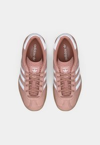 Adidas tenisice u boji prašnjave ruže s bijelim trostrukim dizajnom, vezanjem sprijeda i potplatima od gume, s teksturiranim gornjim dijelom i podstavljenim ovratnikom.