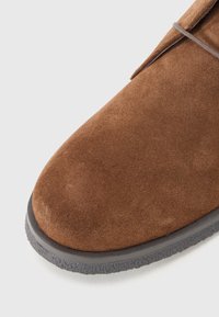 Brown suede shoe with a rounded toe, gray rubber sole, and minimal stitching detail. Smooth texture with a soft appearance.