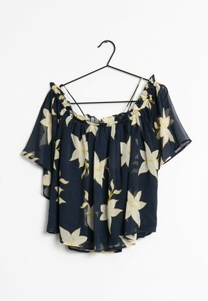 Granatowa bluzka typu 'off-shoulder' z białym kwiatowym nadrukiem, krótkimi rękawami i marszczonym elastycznym dekoltem, wisząca na czarnym wieszaku.