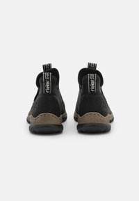 Zwarte enkellaarzen met een leren bovenkant met textuur, contrasterende bruine zool en trekriemen voor eenvoudig aan- en uittrekken. Rondgevormd met een gevoerde hak.