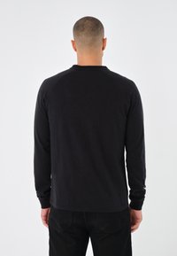 Langärmliges schwarzes Shirt mit geripptem Rundhalsausschnitt und Raglanärmeln, aus einem weichen Stoff gefertigt, mit geradem Saum und minimalen Details.