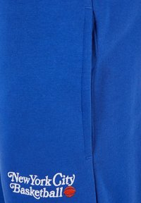 Blå bomullssweatpants med sidelommer og brodert tekst "New York City Basketball" med en detalj av en basketball.