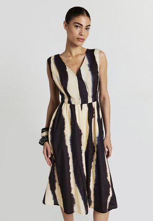 Ein ärmelloses Kleid mit V-Ausschnitt, aus Stoff mit gelben und dunkelbraunen Batikstreifen, tailliert für eine ausgestellte Silhouette.