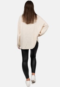Camicia a maniche lunghe color crema con tessuto strutturato e pois bianchi, abbinata a leggings neri lucidi e sneaker bianche. Vista da dietro.