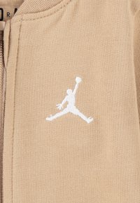Beige Zip-Hoodie mit einem weißen gestickten Jumpman-Logo. Der Stoff wirkt weich und hat ein strukturiertes Strickmuster.