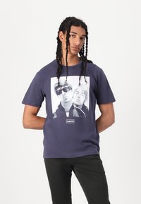 Navy blue cotton t-shirt featuring a bold black and white graphic of two figures. Text "oasis" below the image. Short sleeves, crew neck.