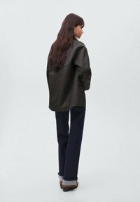 Črna, prevelika jakna z nežnim leskom, nosena čez temne hlače; ima sproščen kroj in stranske žepke, prikazuje teksturirano tkanino.