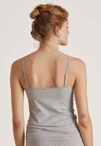 Grijze, aangesloten top met dunne bandjes, gemaakt van zachte stof. Gladde textuur, minimalistisch ontwerp, met een kleine tatoeage op de arm.