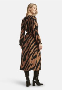 Bruin en zwart gestreepte lange mouw jurk met een cinched taille, gemaakt van een lichte stof. Draag met zwarte kniehoge laarzen.