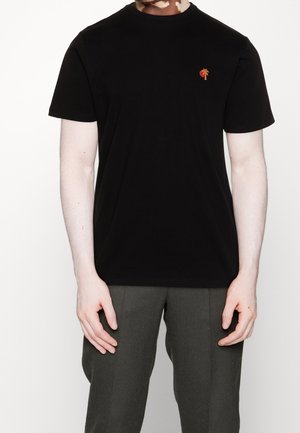 Camiseta negra de algodón con mangas cortas y cuello redondo. Presenta un pequeño logo bordado de una palmera en el lado izquierdo del pecho.