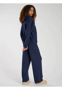 Felpa blu navy e pantaloni larghi realizzati in morbido materiale. La felpa presenta un semplice logo sulla parte anteriore, con una vestibilità comoda.
