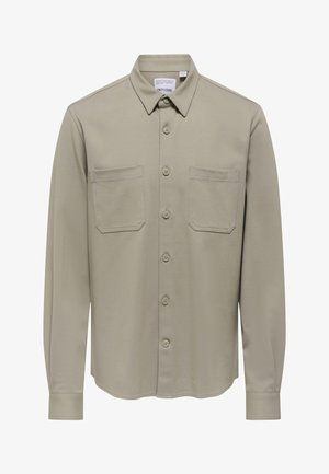 Camicia kaki con bottoni, colletto, due tasche sul petto e maniche lunghe. Tessuto liscio con una vestibilità su misura e dettagli di cuciture sottili.