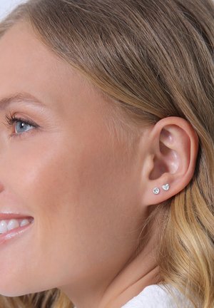 Boucles d'oreilles en argent avec un design en pierre ronde et en forme de cœur, portées sur l'oreille d'un mannequin. Design simple, élégant et minimaliste.