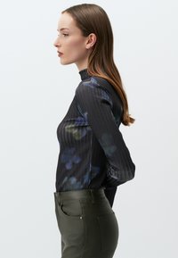 Zwarte en gemusterde blouse met lange mouwen met verticale strepen en bloemaccenten, gecombineerd met olijfgroene slim-fit broeken.