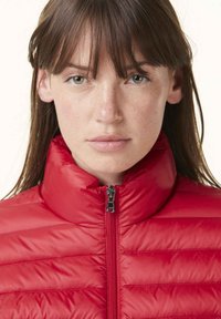 Giacca imbottita rossa con colletto alto, texture trapuntata e zip completa. Materiale morbido con un leggero lucido; design minimale senza motivi o dettagli visibili.