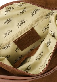 Wnętrze brązowej torebki z zamszu z jasnosłoną podszewką z powtarzającym się logo "VENEZIA", w tym kieszeń na zamek i miękka tekstura.