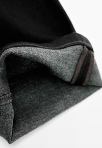 Zwarte en grijze stoffen manchet met een gladde textuur, gevouwen om contrasterende lagen te onthullen. Heeft zichtbare stiksels en een verstevigde rand.