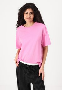 T-shirt en coton rose à manches courtes ; coupe décontractée. Associé à un pantalon de jogging noir à rayures blanches avec une ceinture à cordon blanc.