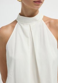 Haut halter blanc avec un col haut et un design plissé, présentant une texture lisse et un style minimaliste. Aucun matériel ou accent visible.