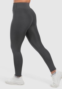 Leggings neri a vita alta realizzati in materiale elasticizzato, caratterizzati da una texture liscia e un design aderente, abbinati a scarpe da ginnastica bianche.