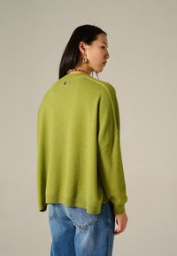 Maglione verde di grandi dimensioni con orlo e polsi a coste, realizzato in morbido tessuto a maglia. Abbinato a jeans di denim azzurro chiaro, caratterizzati da una vestibilità rilassata.