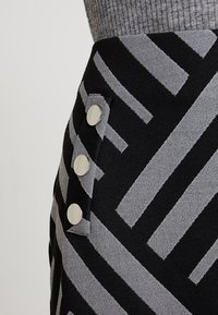 Jupe noire et grise à motif avec des rayures horizontales et diagonales. Présente des boutons en argent sur le côté. Le tissu a une apparence texturée.