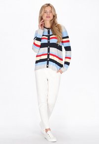 Csíkos kardigán kék, szürke, piros és fekete színekben, gombokkal az elején. Fehér nadrággal és fehér tornacipővel párosítva.