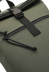 Sac à dos imperméable vert avec fermeture éclair et sangle noires, doté d'une fermeture à boucle sur le dessus et d'une surface texturée. Comprend un cordon de serrage réglable.