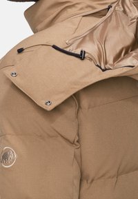 Béžová péřová bunda s texturovaným povrchem, saténovou podšívkou, kapsou na zip a logem slona na rukávu.