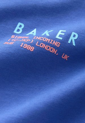 Modrá bavlněná tkanina s potiskem textu v světle modré a oranžové: "BAKER SIGNAL INCOMING (TC-JKP) LONDÝN, UK 1988" vykazuje hladkou texturu.