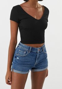 Svart ribbat kortärmad topp med djup V-ringning, tillsammans med blå denimshorts med uppvikt fåll och slitet utseende.