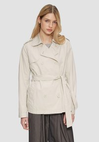 Beige doppeltknöpfiger Trenchcoat mit einem taillierten Gürtel, Schulterklappen und zwei vorderen Taschen; aus leichtem Stoff gefertigt.