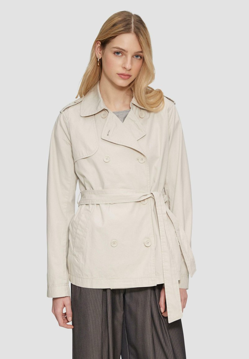 Beige doppeltknöpfiger Trenchcoat mit einem taillierten Gürtel, Schulterklappen und zwei vorderen Taschen; aus leichtem Stoff gefertigt.