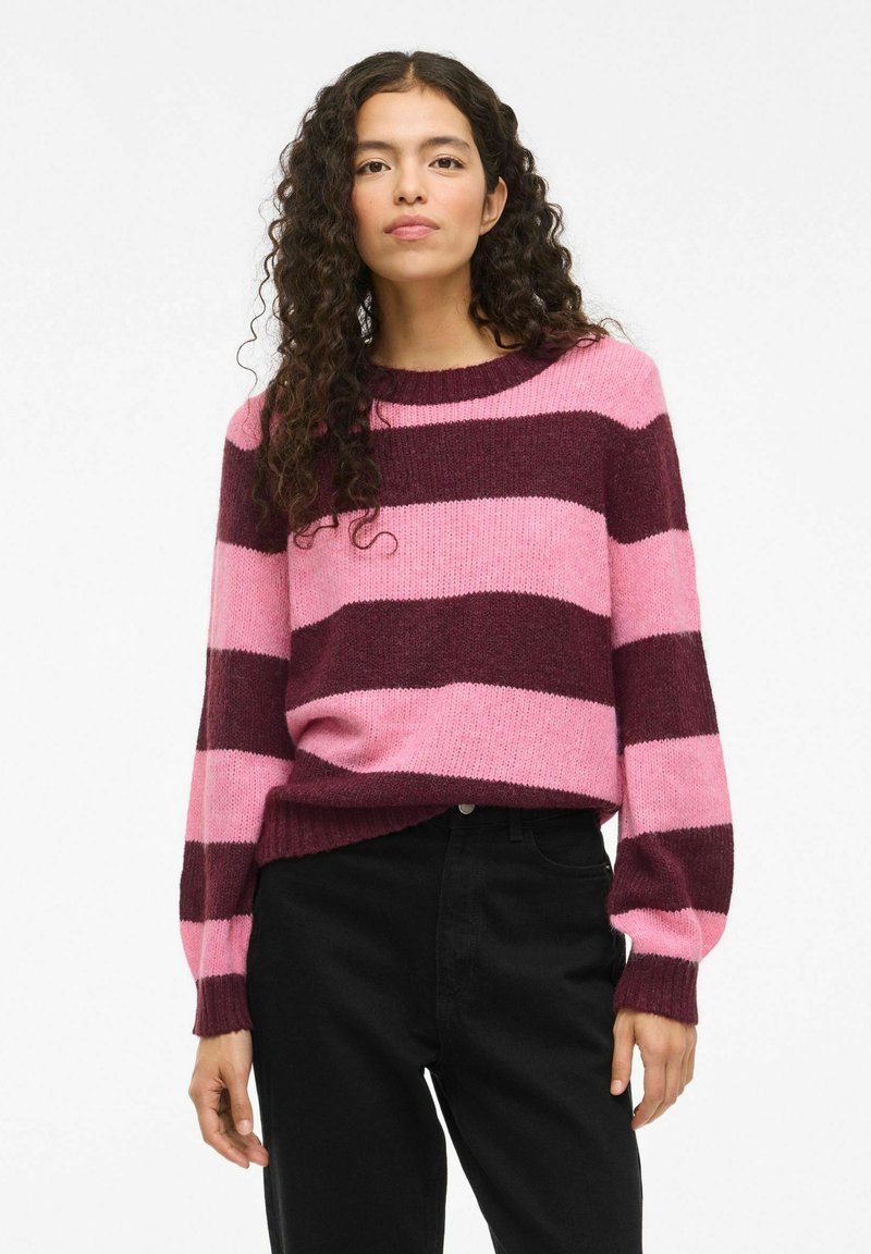 Lila und rosa gestreifter Strickpullover mit Rundhalsausschnitt, geripptem Saum und Bündchen, kombiniert mit schwarzen Hosen, die eine weiche Textur zeigen.