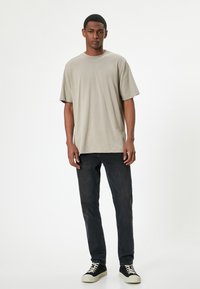 Camiseta de algodón beige con cuello redondo y corte relajado. Combinada con jeans oscuros y zapatillas negras con suelas y cordones blancos.