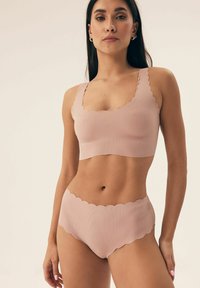 Light pink ribbed bralette with scalloped edges, paired with matching scalloped panties. Soft fabric and seamless design.