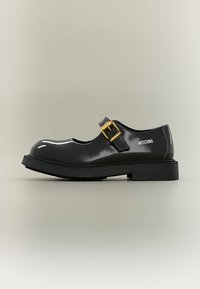 Chaussure Mary Jane noire brillante avec semelle épaisse, bride à boucle dorée et logo Moschino sur le côté, vue de profil sur fond neutre.