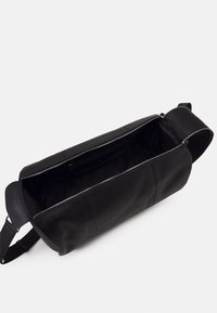 Svart läderväska med en texturerad yta och en stor öppning. Har en silverfärgad dragkedja och ett brett rem för enkel bärning.