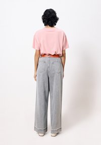 Roze t-shirt met korte mouwen; lichtgrijze wijde jeans met gescheurde zoom; oranje riem. Achteraanzicht van een casual outfit.