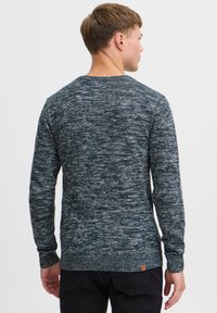 Mørkeblå og grå melert genser med rund hals, ribbestrikkede ermer og kant; har et lite lærmerke på nedre rygg.