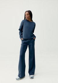Niebieska, dopasowana bluza i szerokie spodnie wykonane z miękkiego materiału o gładkiej fakturze. Góra ma okrągły dekolt i luźny krój.
