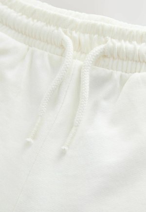 Valged fliisist lühikesed püksid, millel on elastne vöökoht reguleeritavate nööridega. Sile tekstuur ja lihtne disain, nähtavate mustriteta.